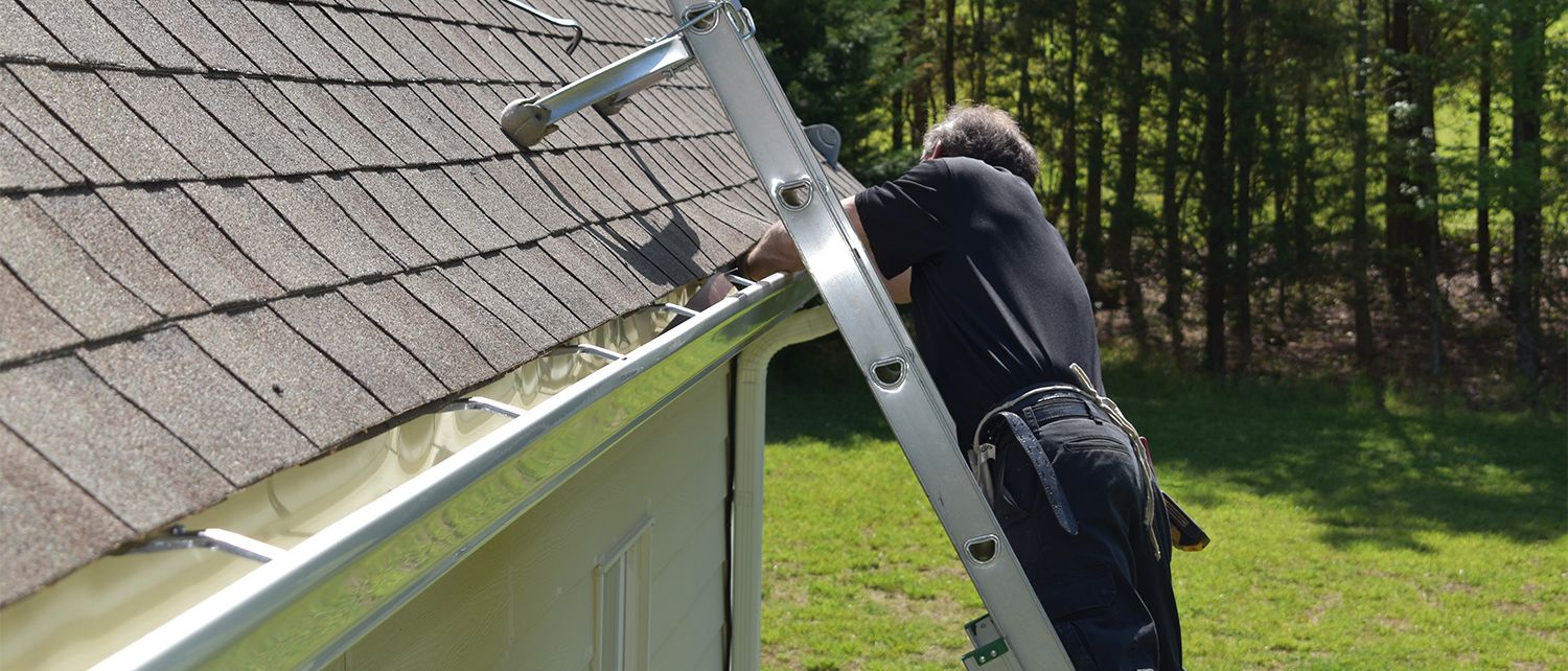 man on a ladder installing gutters